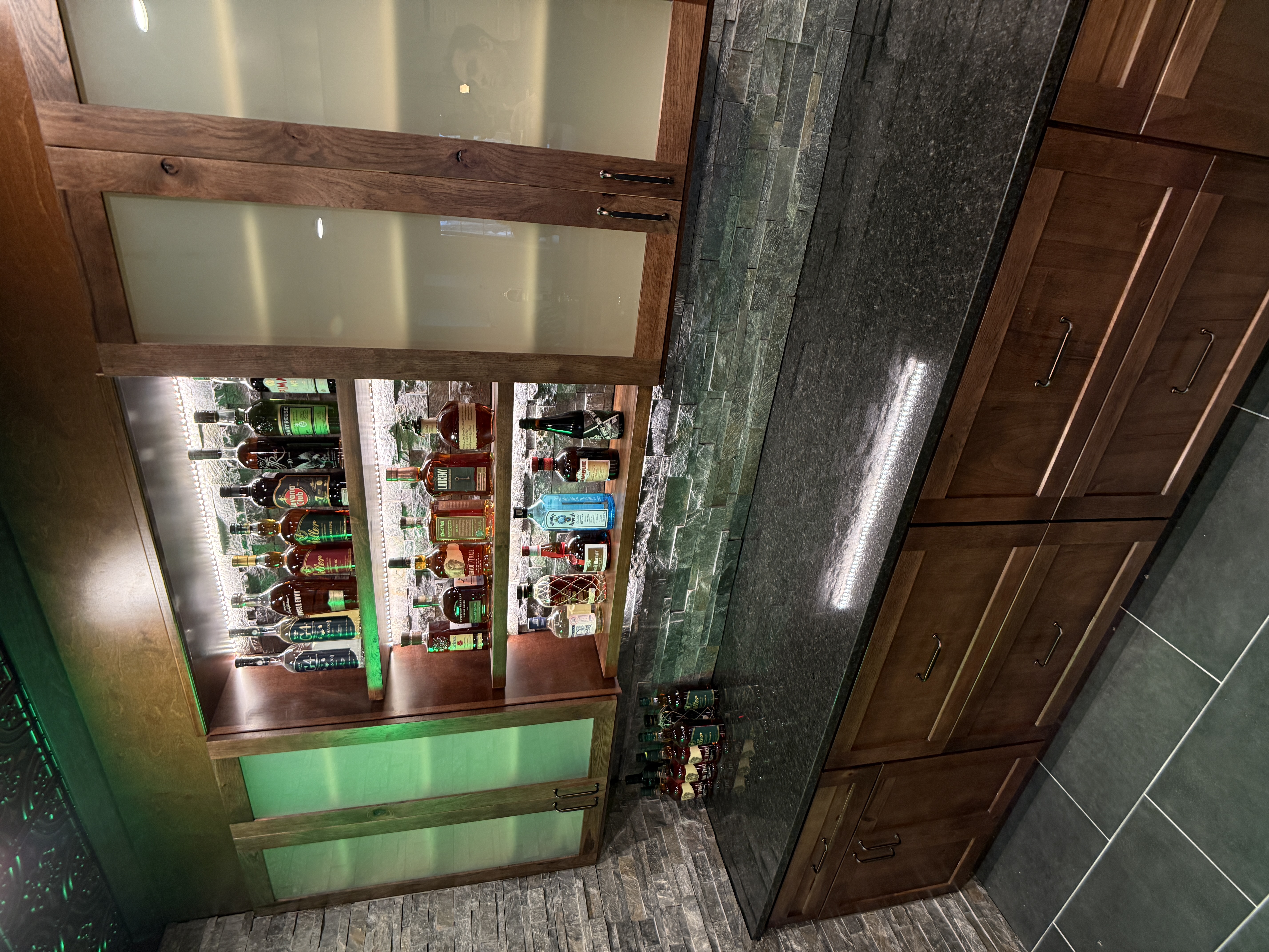 Basement bar with backlit liquor display and custom wood cabinetry by Serge Construction