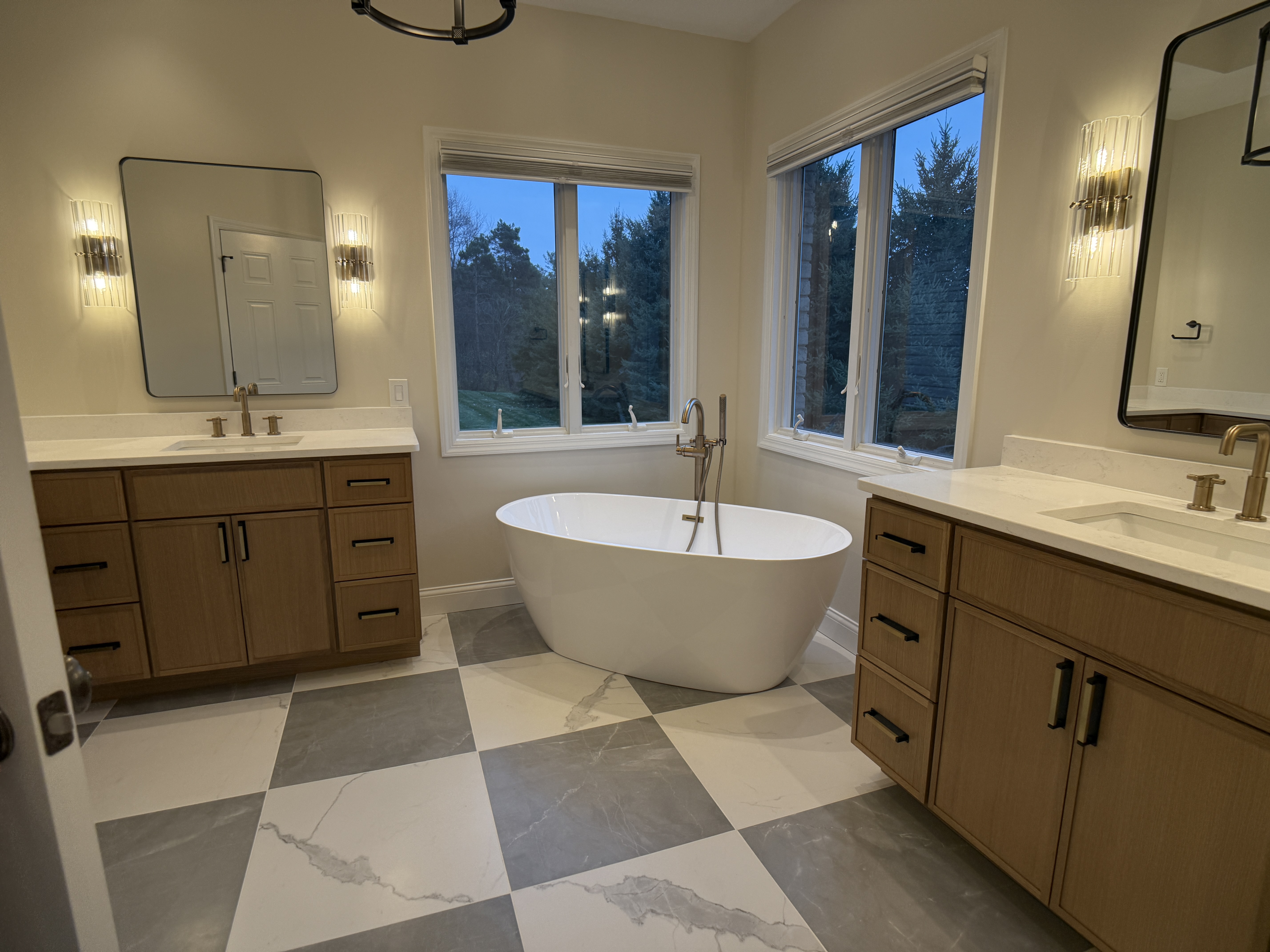 Master bathroom with dual wood vanities and freestanding soaking tub by Serge Construction